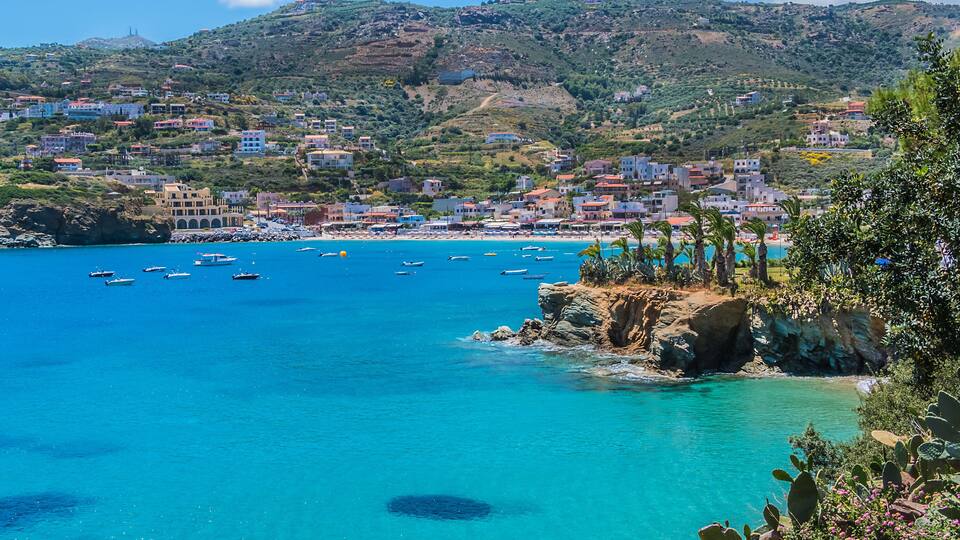 A coastal town with clear turquoise waters, boats, and buildings on a hillside.