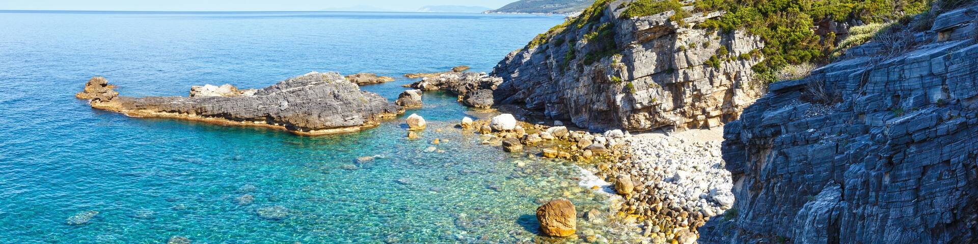 A coastal landscape with clear blue waters, rocky formations, and a cliff with vegetation.