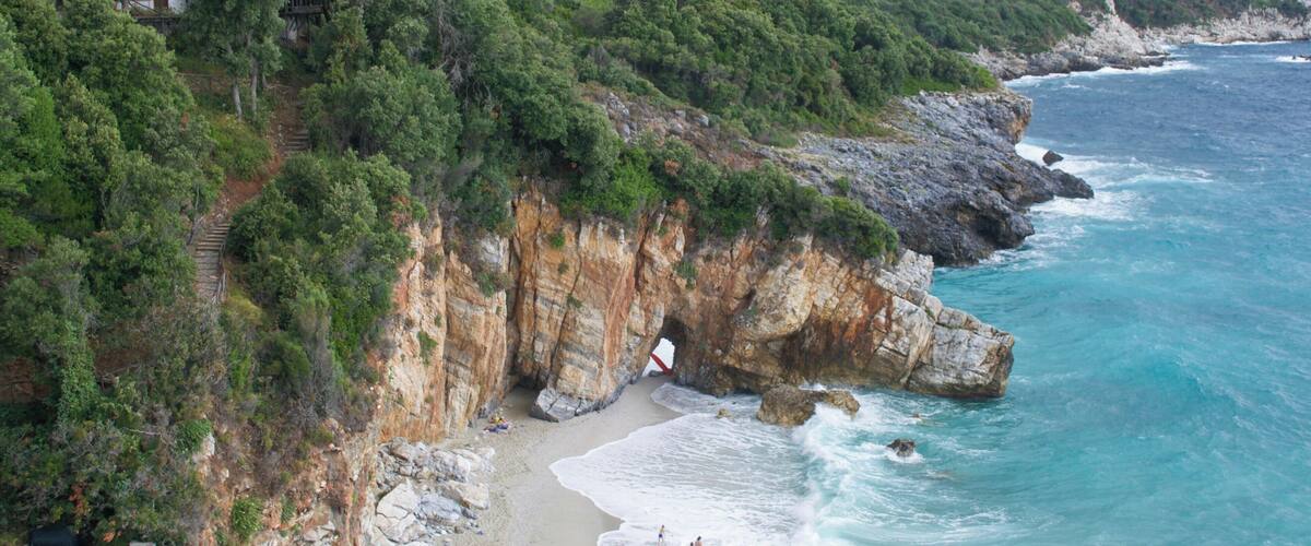 A coastal landscape with a rocky beach, cliffs, and a small building on a hillside.