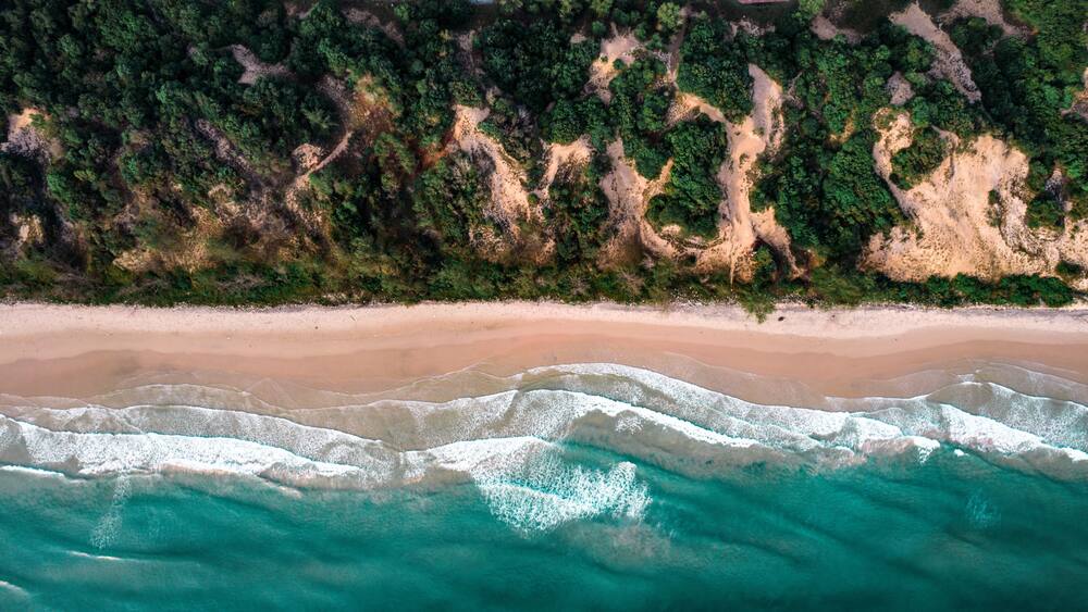 A sandy beach with clear turquoise waters and dense forested cliffs.