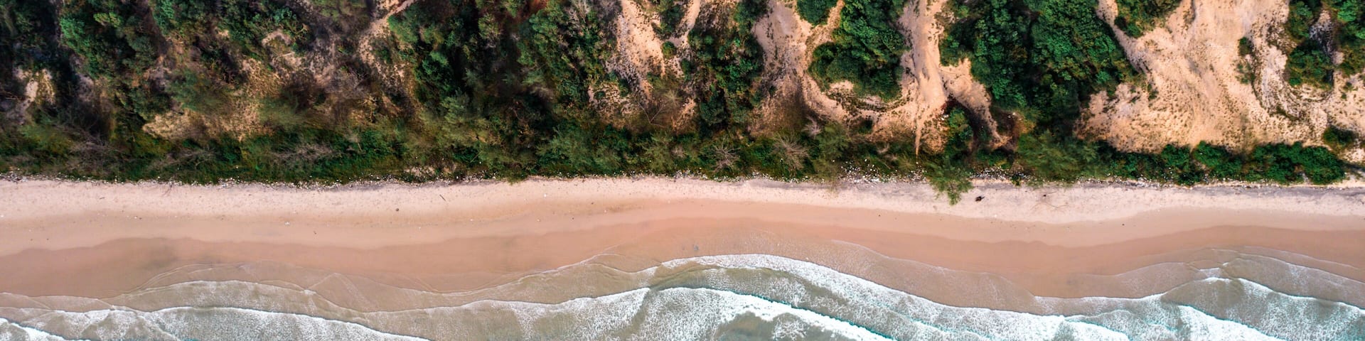 A sandy beach with clear turquoise waters and dense forested cliffs.