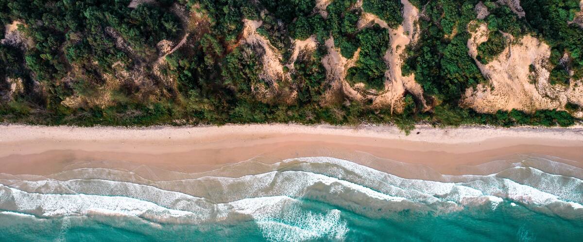 A sandy beach with clear turquoise waters and dense forested cliffs.