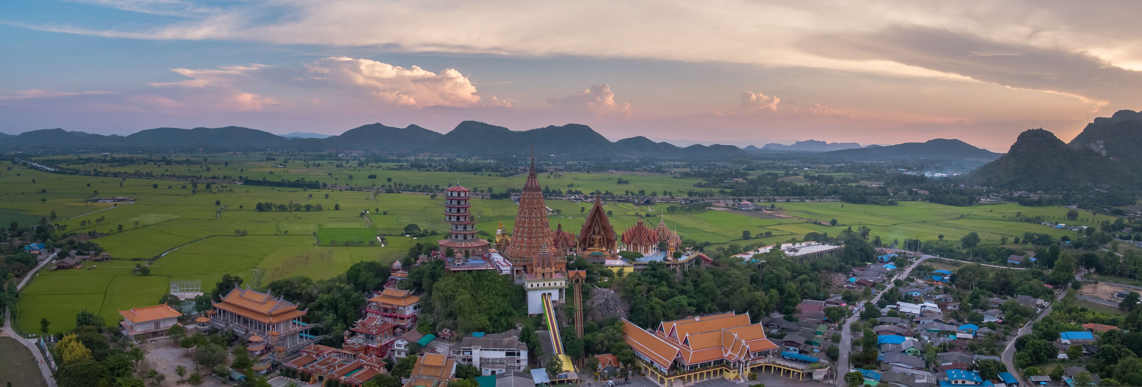 A temple complex with tiered pagodas and traditional architecture amidst green fields and mountains.