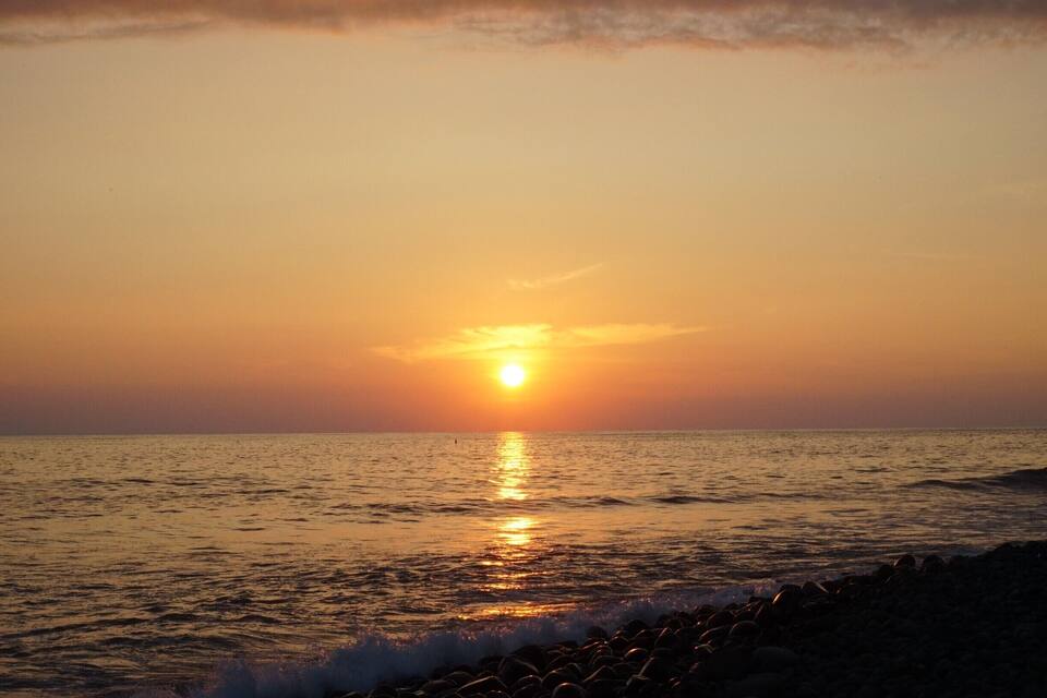 Ein Sonnenuntergang über dem Meer, Wellen schlagen an eine felsige Küste.