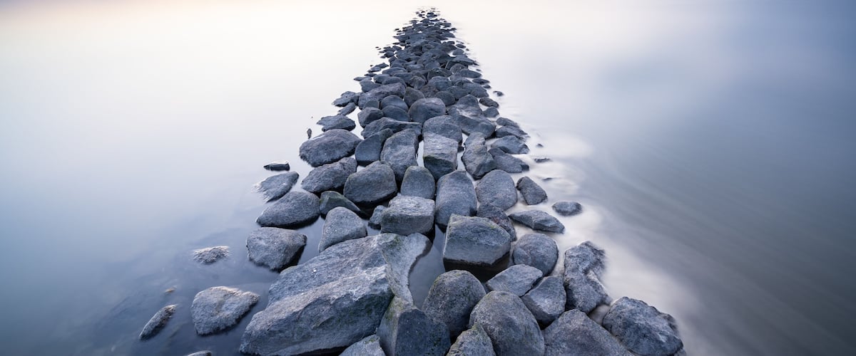 Een lange, smalle stenen pier die zich uitstrekt over kalm water.