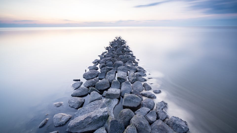 A long, narrow stone pier extending into calm water, surrounded by a serene landscape.