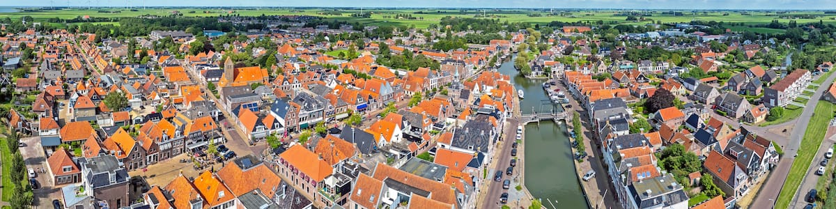 A town with red-roofed buildings, a river, and wind turbines in the distance.