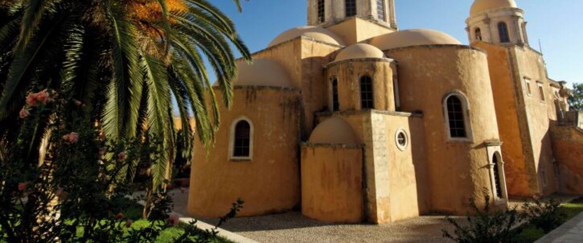 A historic building with multiple domes and arches, surrounded by palm trees and greenery.