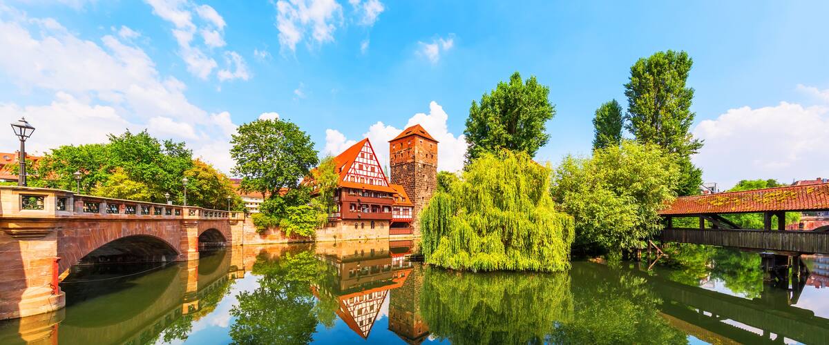 A historic town with a bridge, a tower, and a reflection in the water.