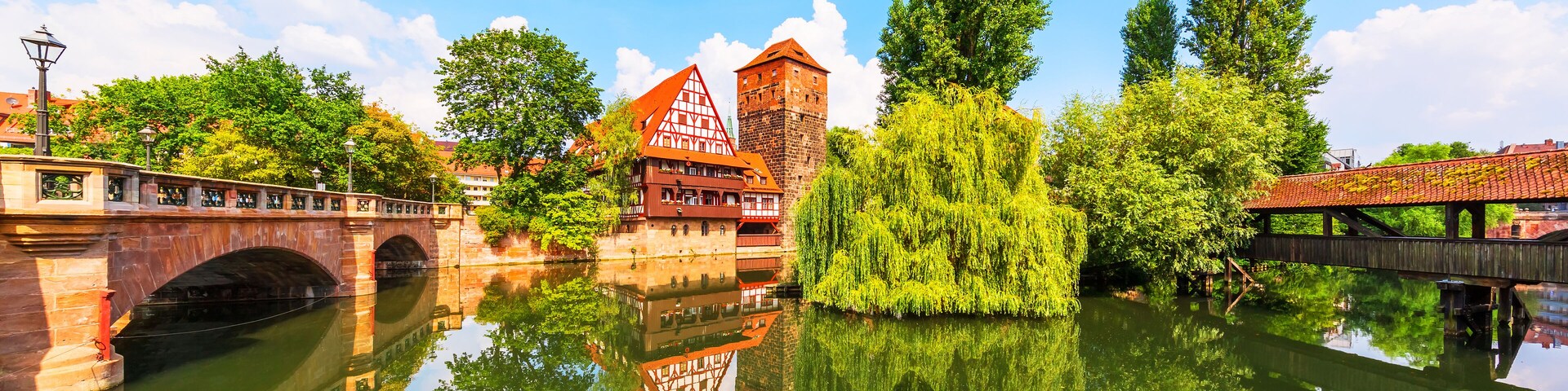 A historic town with a bridge, a tower, and a reflection in the water.