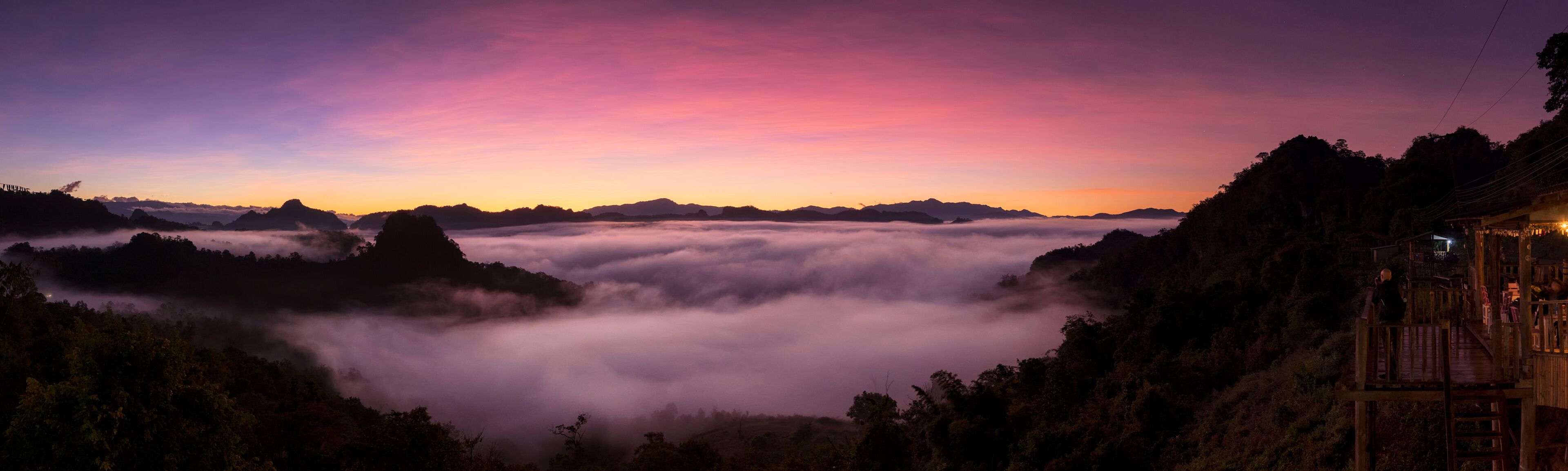 A mountainous landscape at sunset with a wooden structure on the right.
