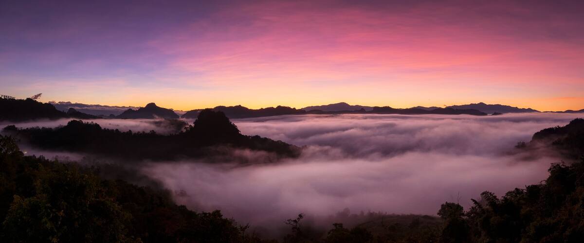 A mountainous landscape at sunset with a wooden structure on the right.