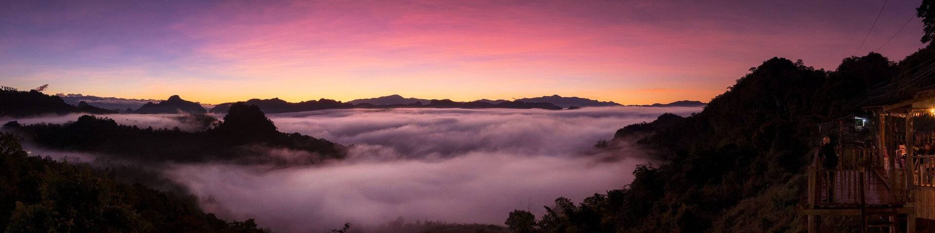 A mountainous landscape at sunset with a wooden structure on the right.