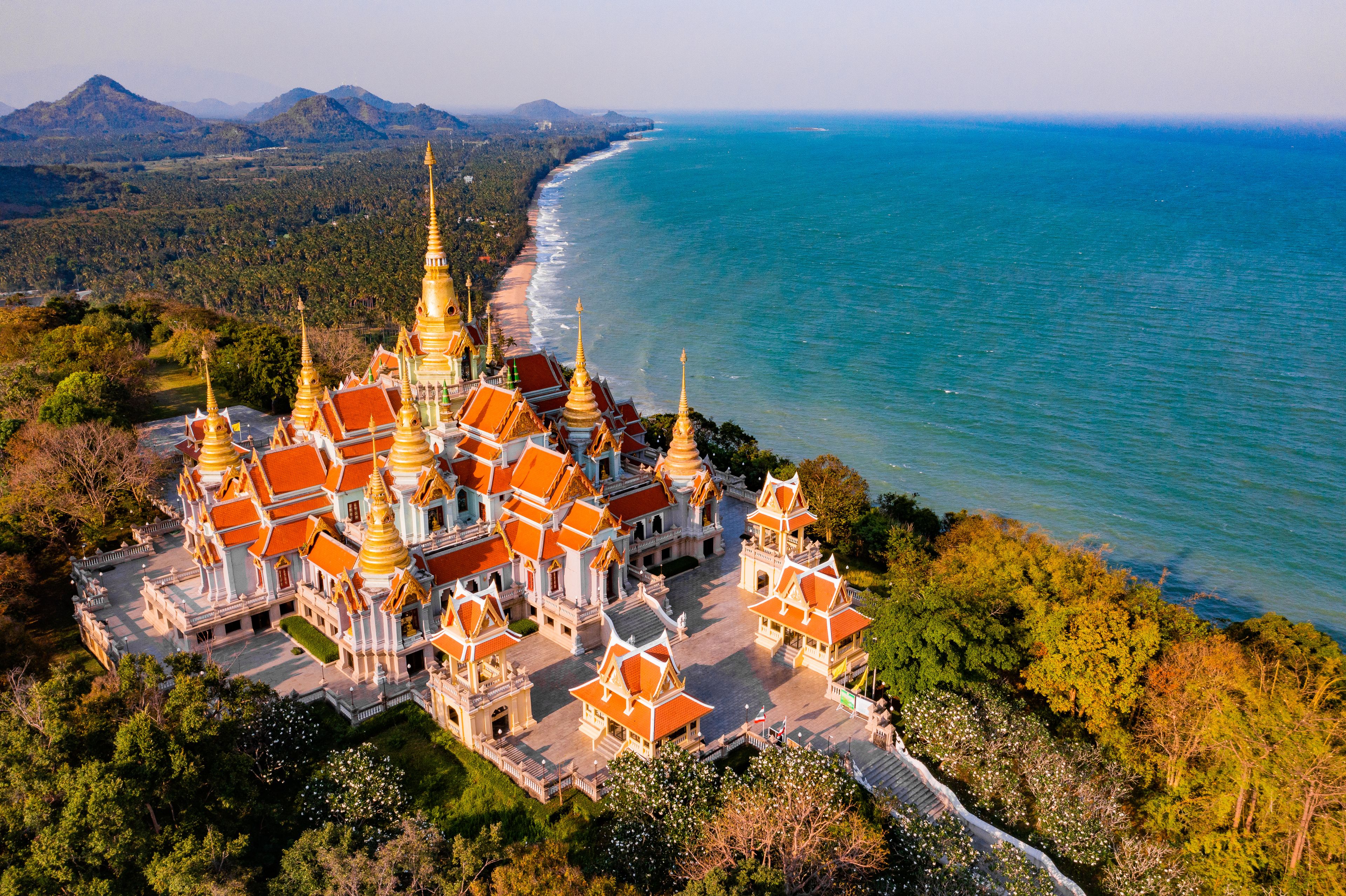 A temple complex with golden spires, red roofs, and a coastline.