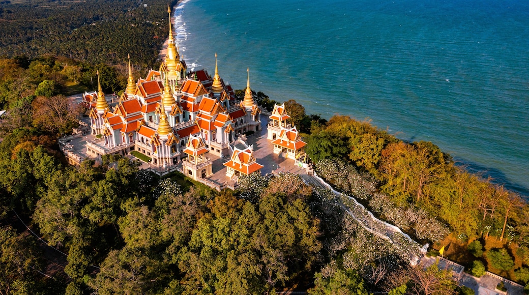 An aerial view of a temple complex with golden spires, surrounded by lush greenery and the coastline.