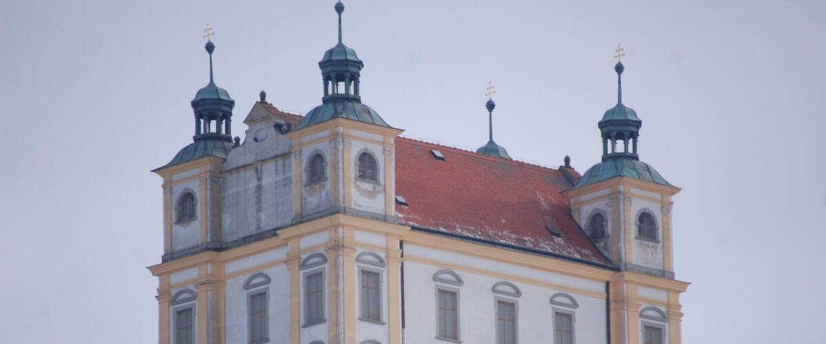 A large, historic building with multiple towers and a red-tiled roof.