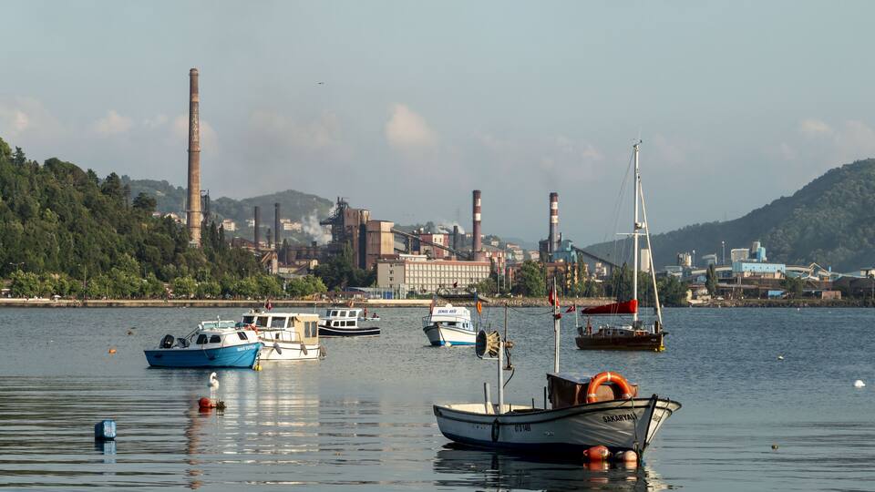A harbor with several boats, a lighthouse, and industrial buildings in the background.