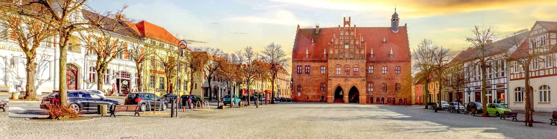 A cobblestone square with historic buildings, a prominent red brick structure, and leafless trees.