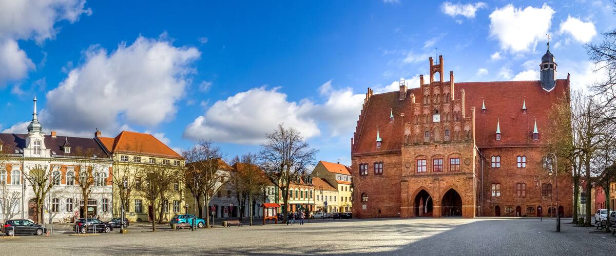 A historic town square with a prominent red brick building and a white church with a spire.