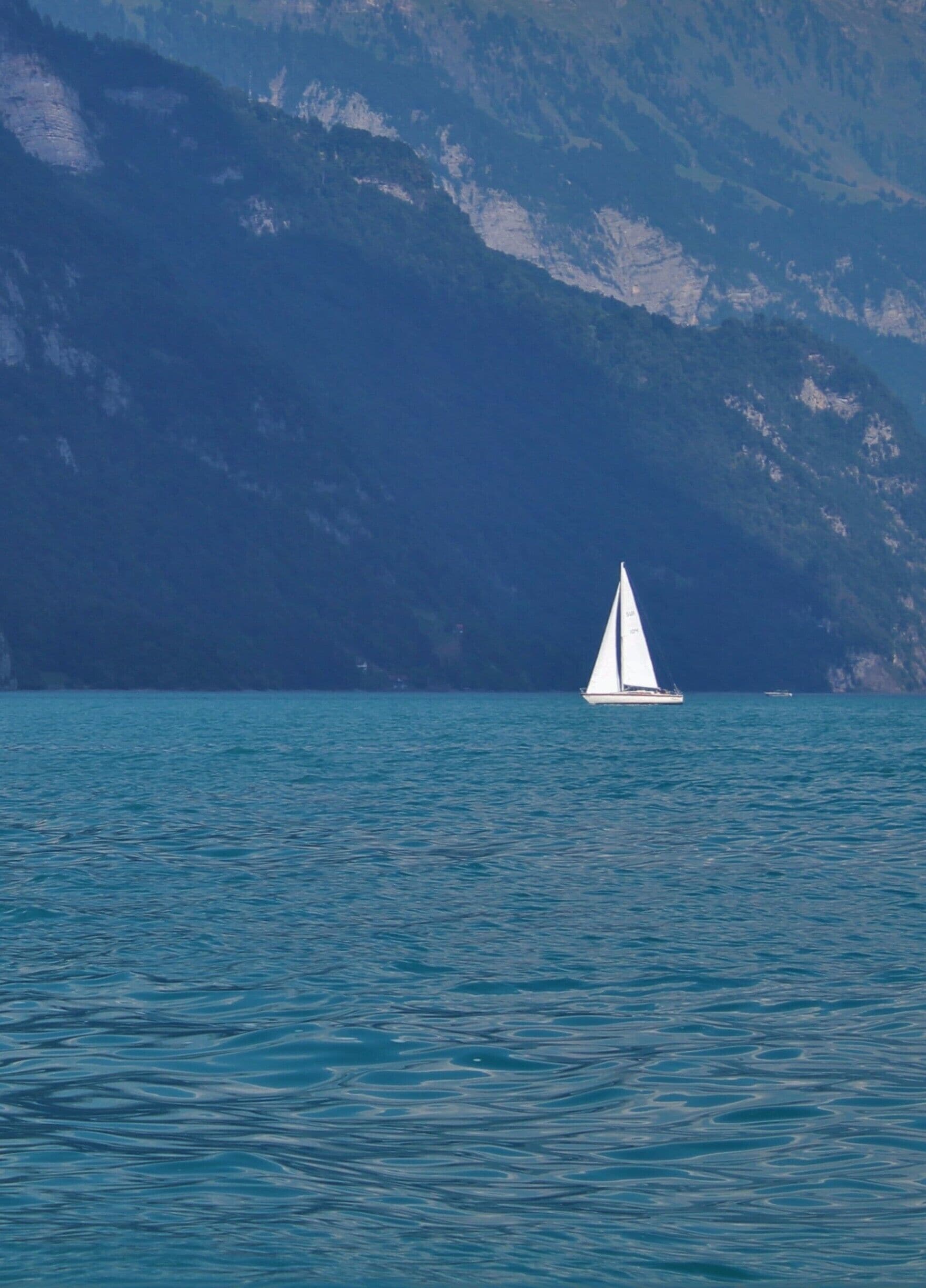 A sailboat on calm waters with a mountainous backdrop.