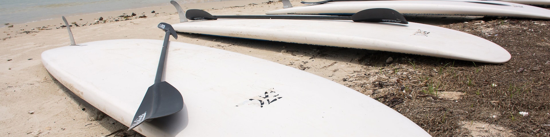 Soft focused of white Surf board on the beach and black surf board paddle on top with Andaman ocean background at Koh Naka Yai,Phuket ,Thailand