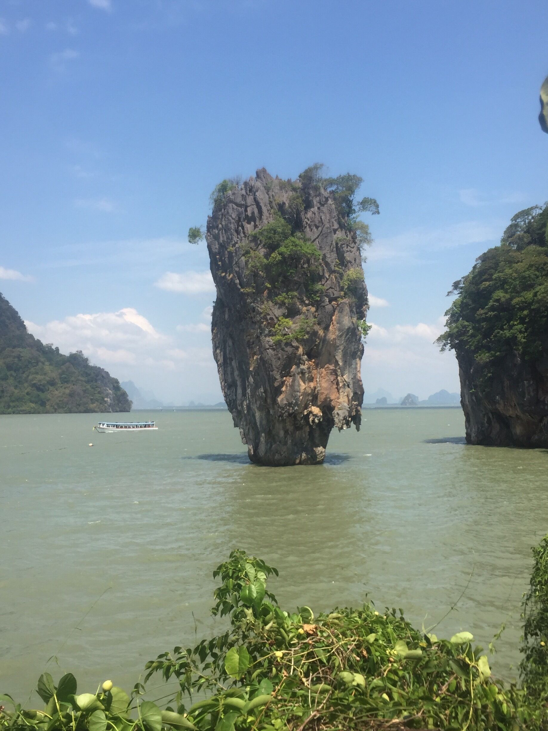 A boat on a calm river with a large rock formation in the center surrounded by greenery.
