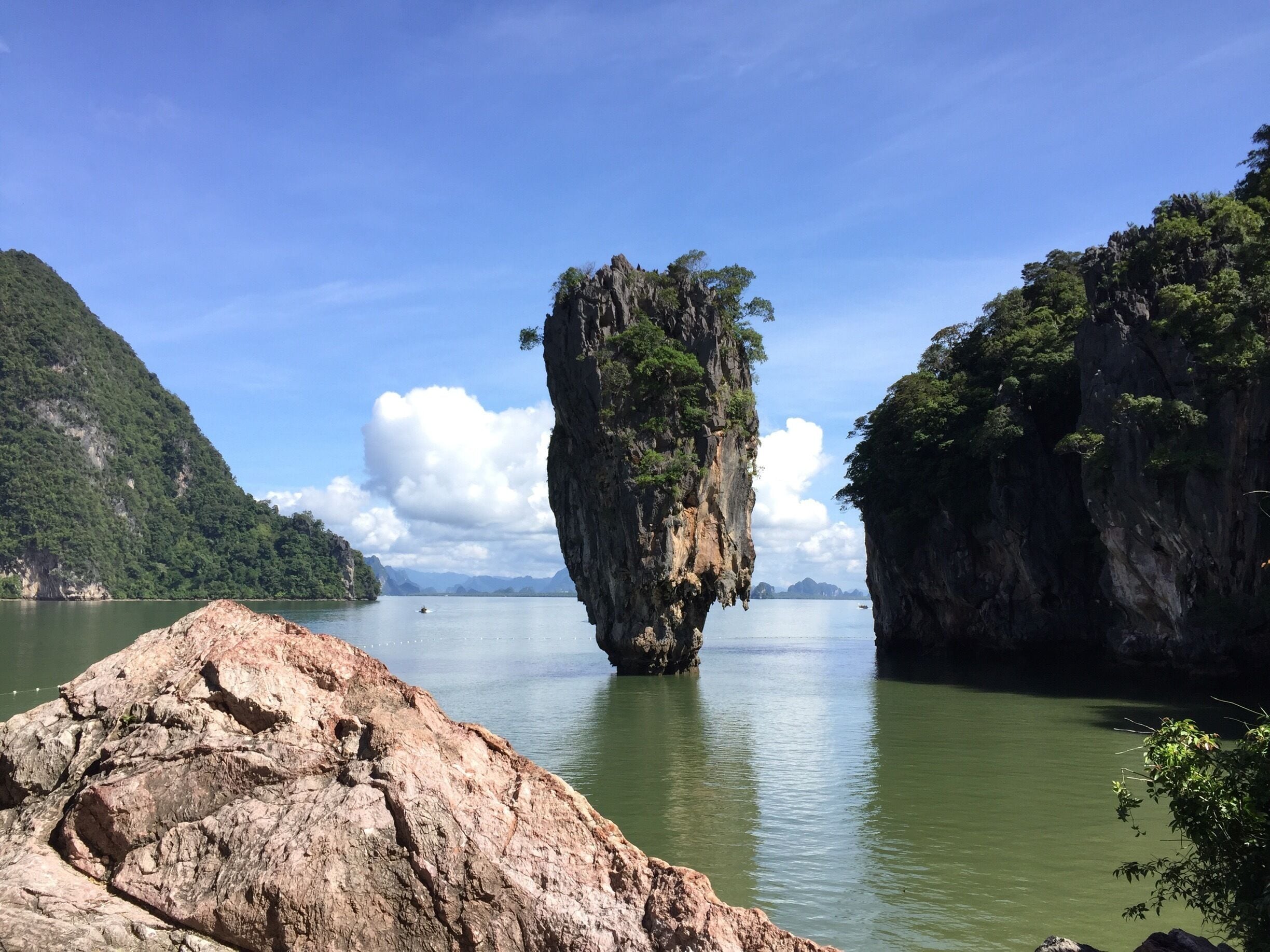 A large rock formation in a body of water surrounded by cliffs.