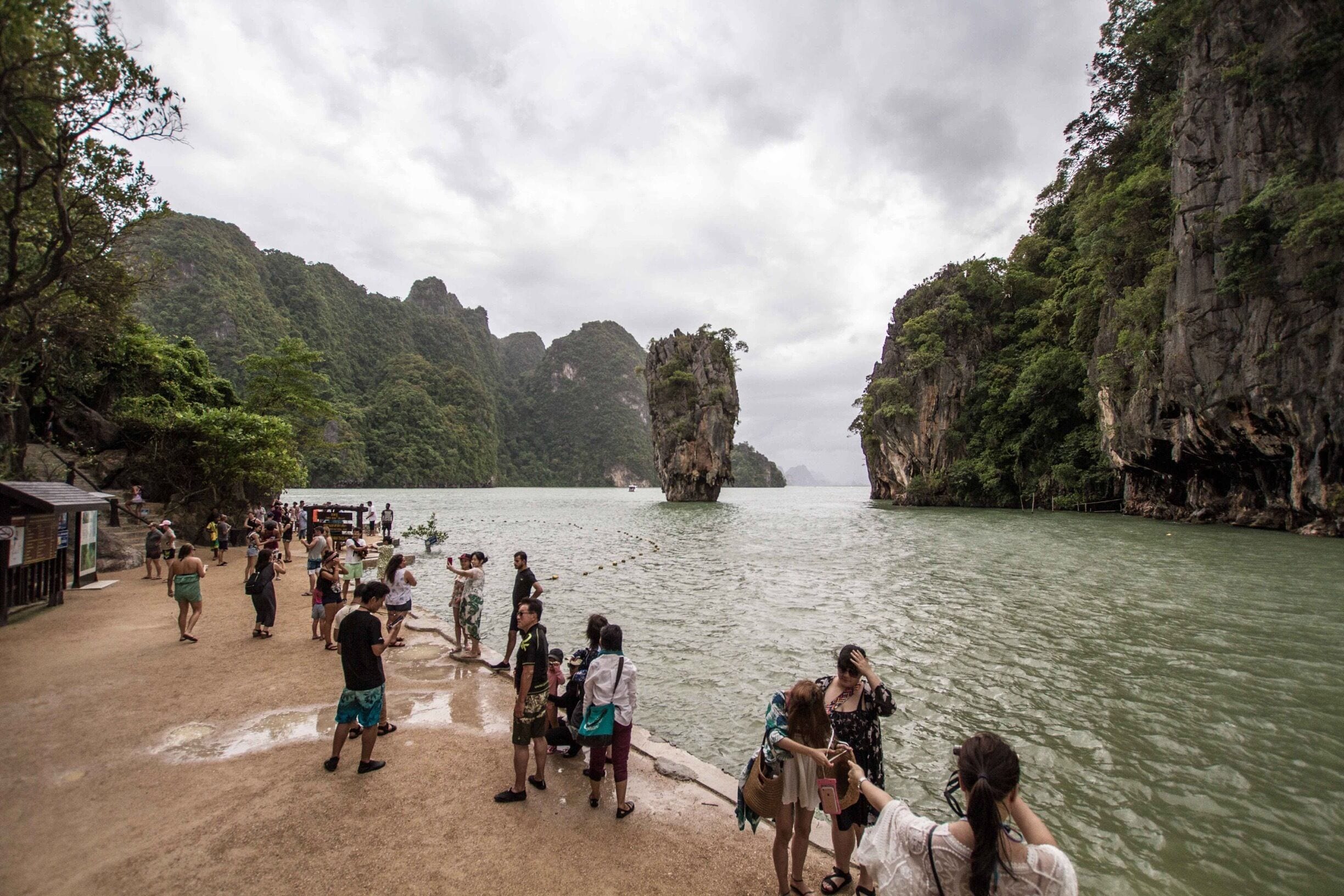 A group of people on a beach with a large rock formation in the water.