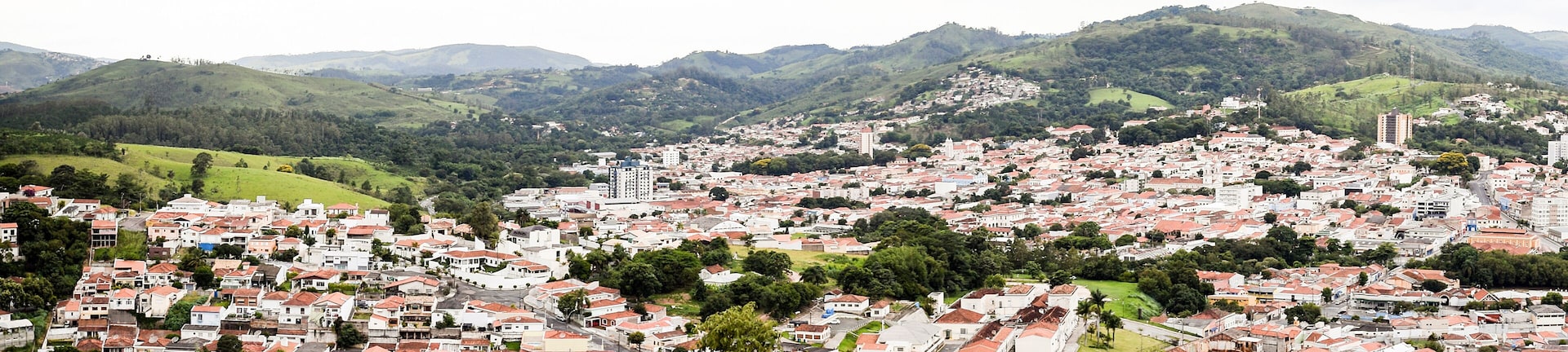 Uma cidade situada num vale, com edifícios de telhados vermelhos, rodeada por colinas e montanhas verdes.
