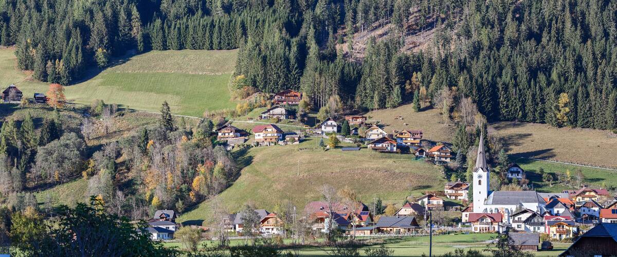 A village nestled in a valley with a church and houses surrounded by forested hills.