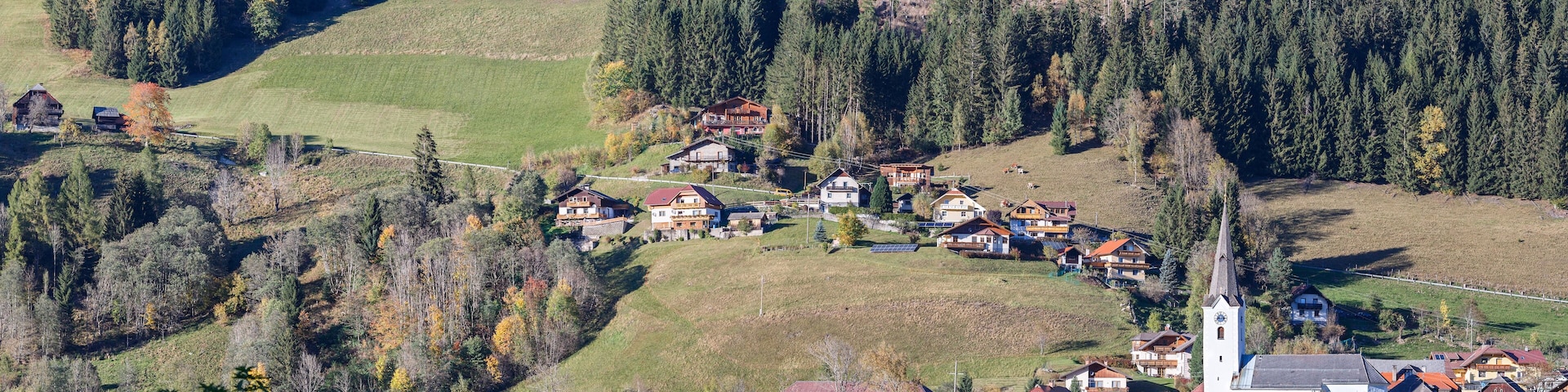 A village nestled in a valley with a church and houses surrounded by forested hills.
