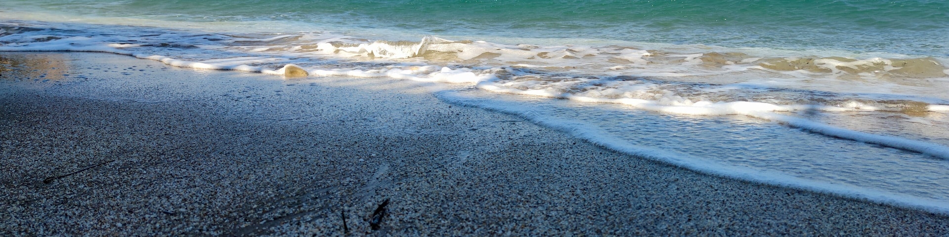 Una playa pedregosa con olas suaves y un mar azul cristalino.