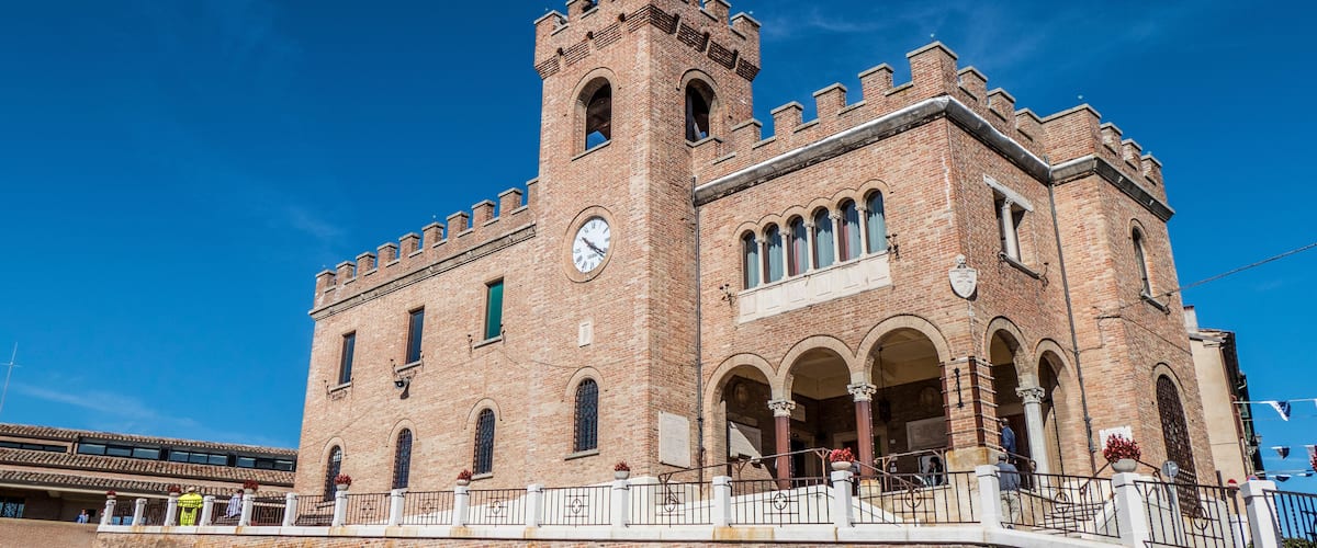 A historic brick building with a clock tower, arched windows, and a flagpole.