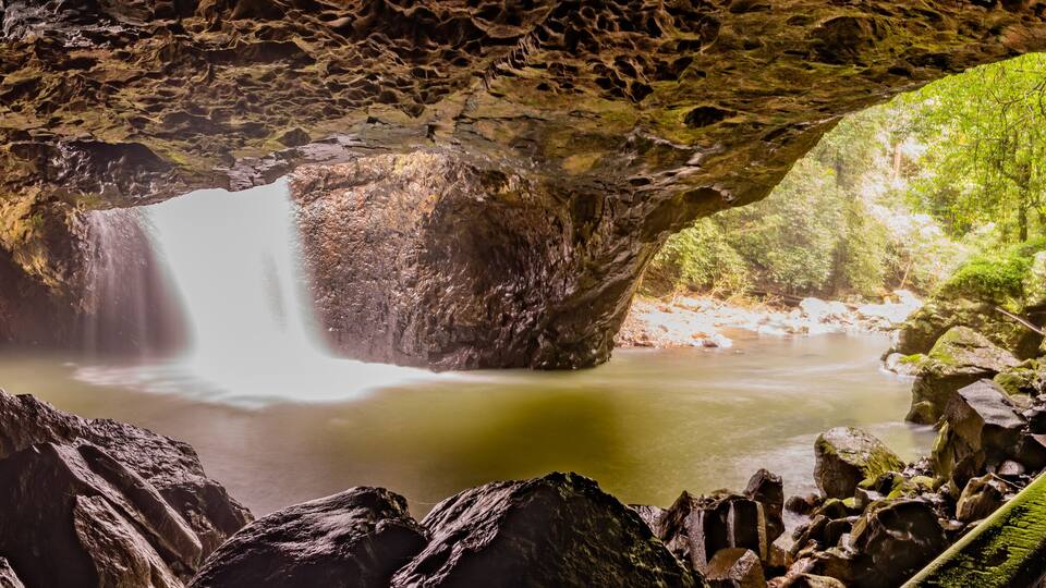 A waterfall in a cave with a wooden staircase leading up.