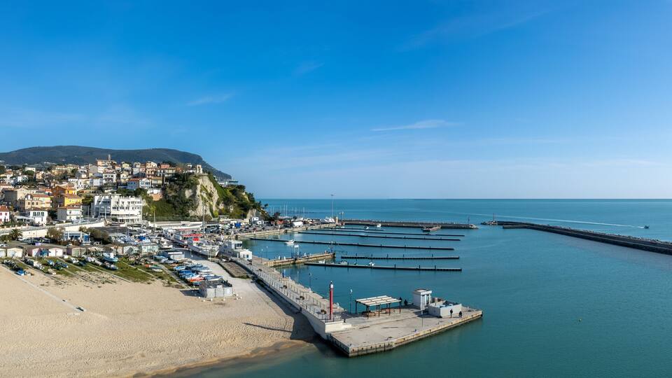 A coastal town with a beach, marina, and buildings on a hillside.