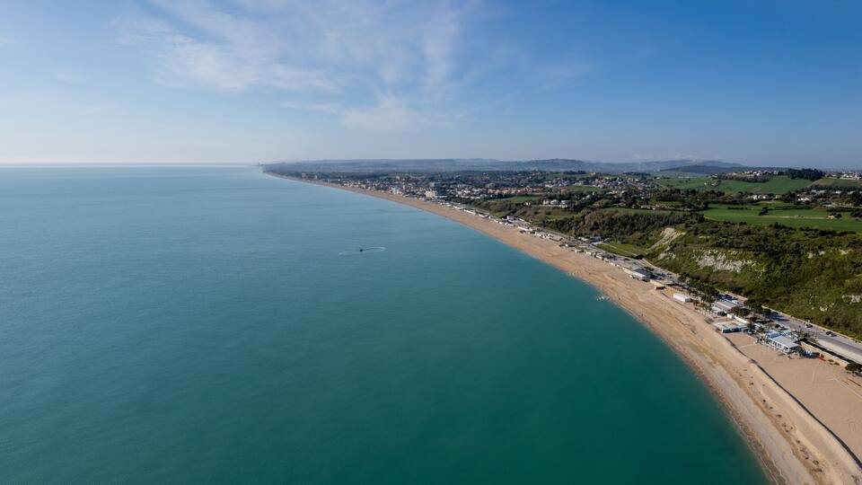 A coastal town with a beach, houses, and greenery along the shoreline.