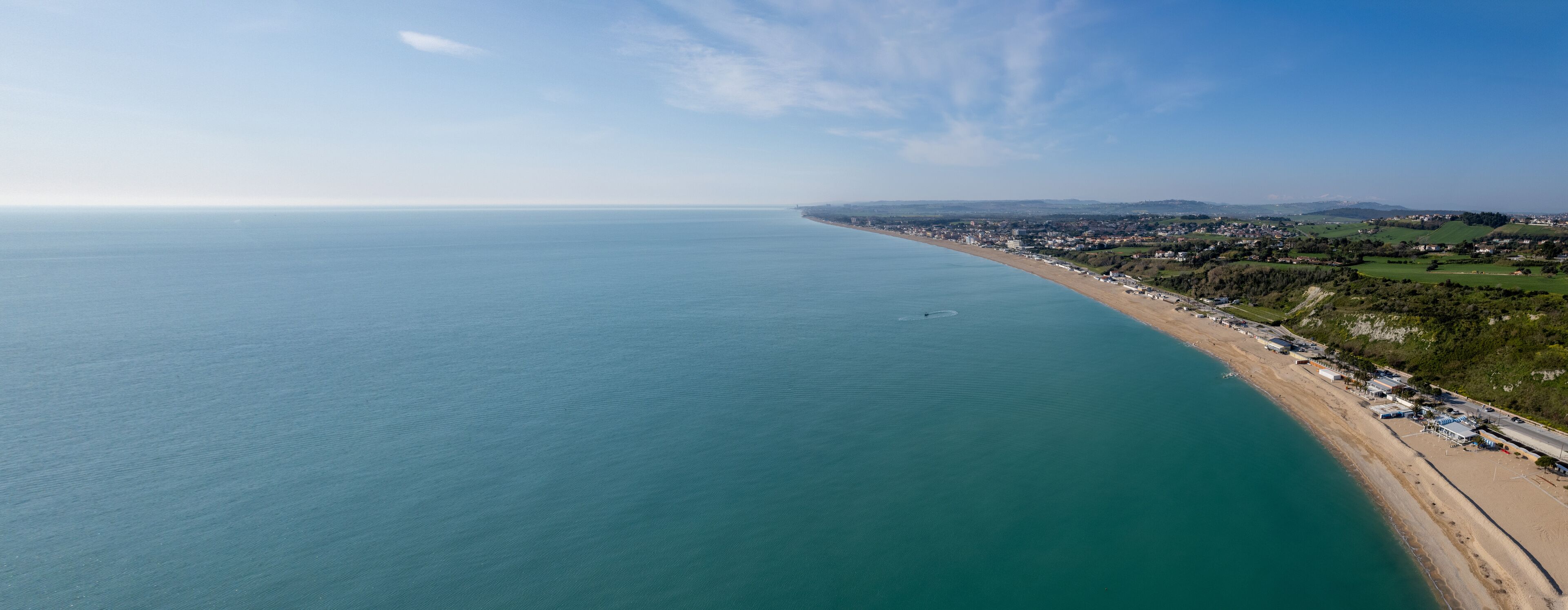 A coastal town with a beach, houses, and greenery along the shoreline.