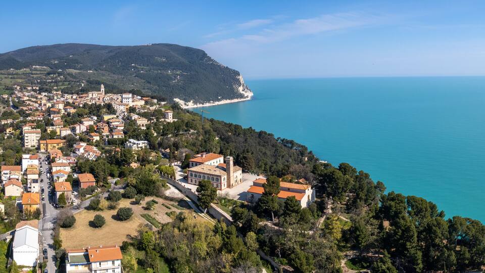 A coastal town with a beach, buildings, and a hill in the background.