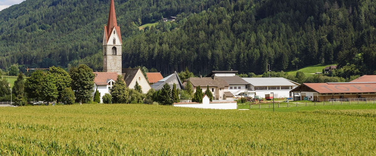 A church with a tall spire, surrounded by houses and fields in a mountainous area.