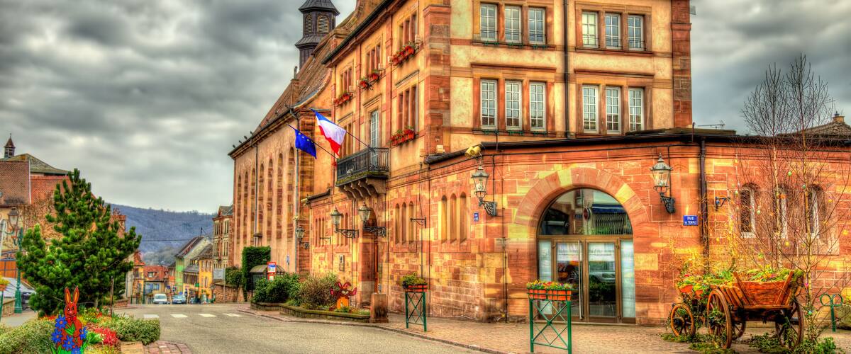 A historic building with a clock tower, flags, and a cobblestone street.