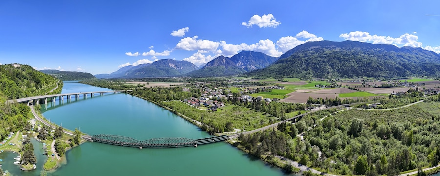 Ein Fluss mit einer Brücke, einer Stadt und Bergen im Hintergrund.