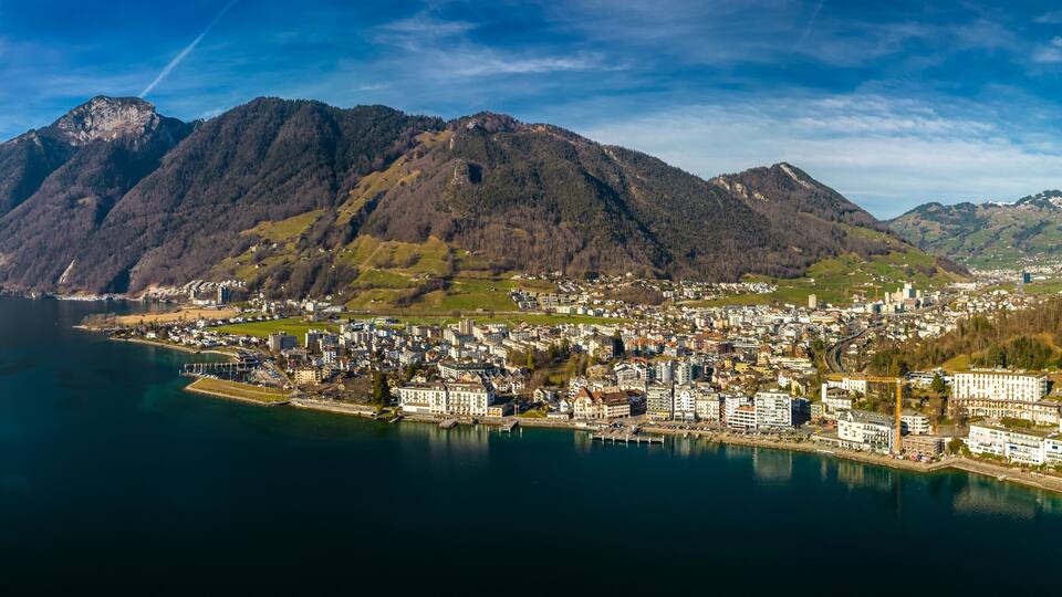A coastal town with a mountain backdrop, a harbor, and a clear sky.