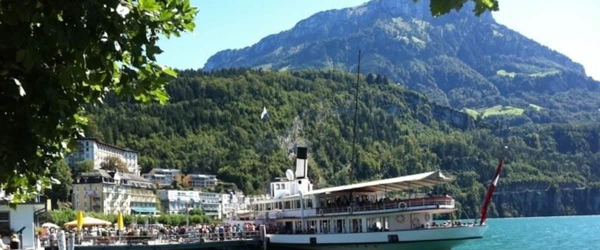 A lake with a boat docked at a pier, surrounded by buildings and a mountain in the background.