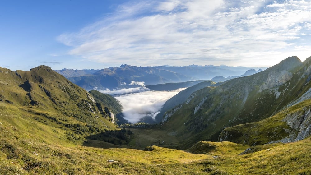 Eine Berglandschaft mit einem Tal, schroffen Gipfeln und blauem Himmel.
