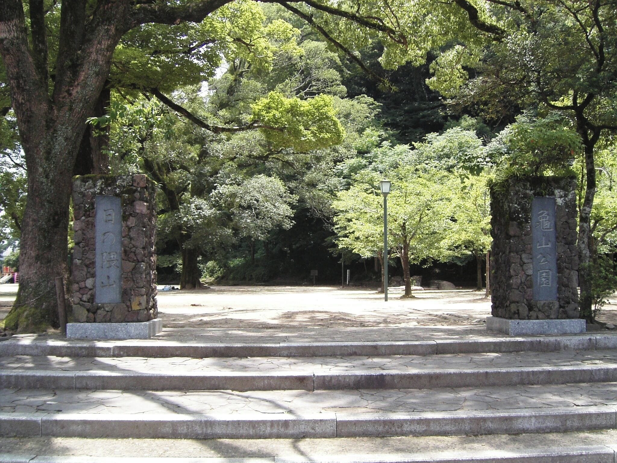 Un sendero de piedra que atraviesa un parque con árboles y pilares de piedra con inscripciones.