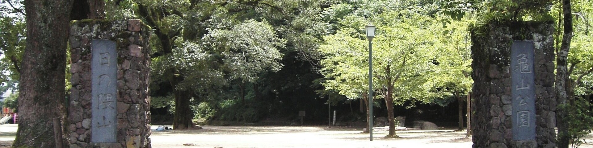 Un sendero de piedra que atraviesa un parque con árboles y pilares de piedra con inscripciones.