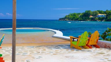 Una playa con piscina, sillas de colores y vistas al océano y una pequeña isla con casas.