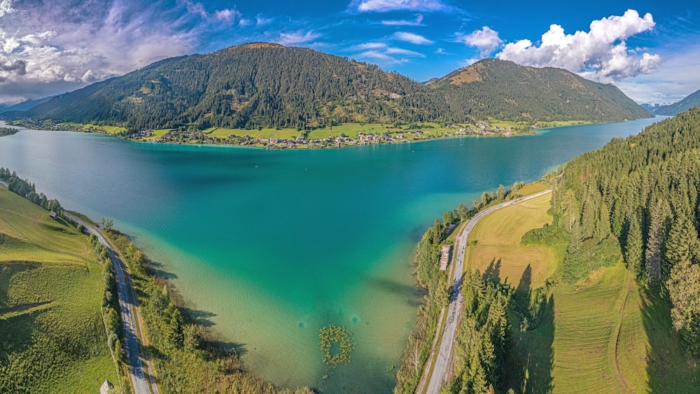 Ein See, umgeben von bewaldeten Hügeln und einer kurvigen Straße.