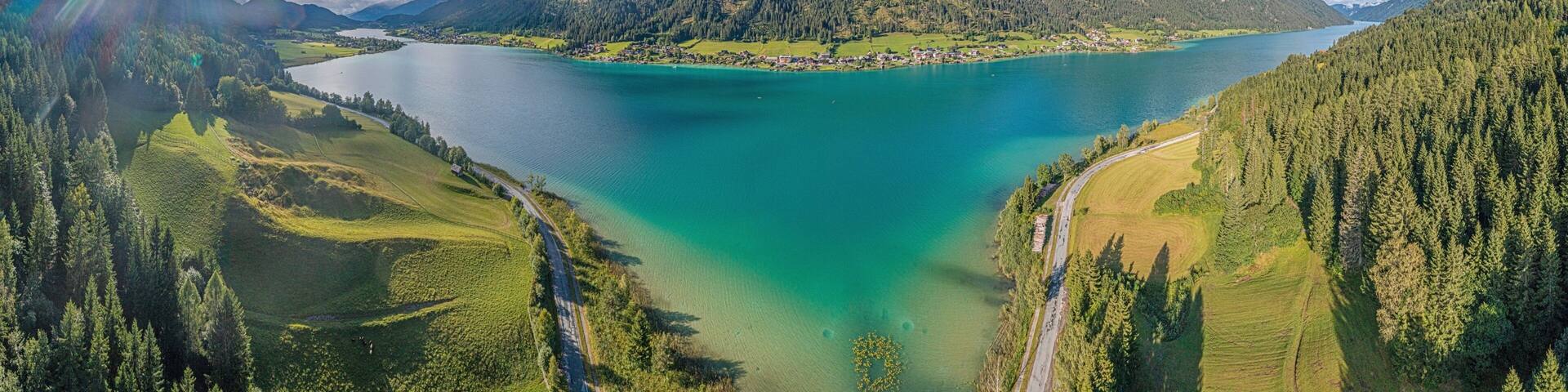 A lake surrounded by forested hills and a winding road.