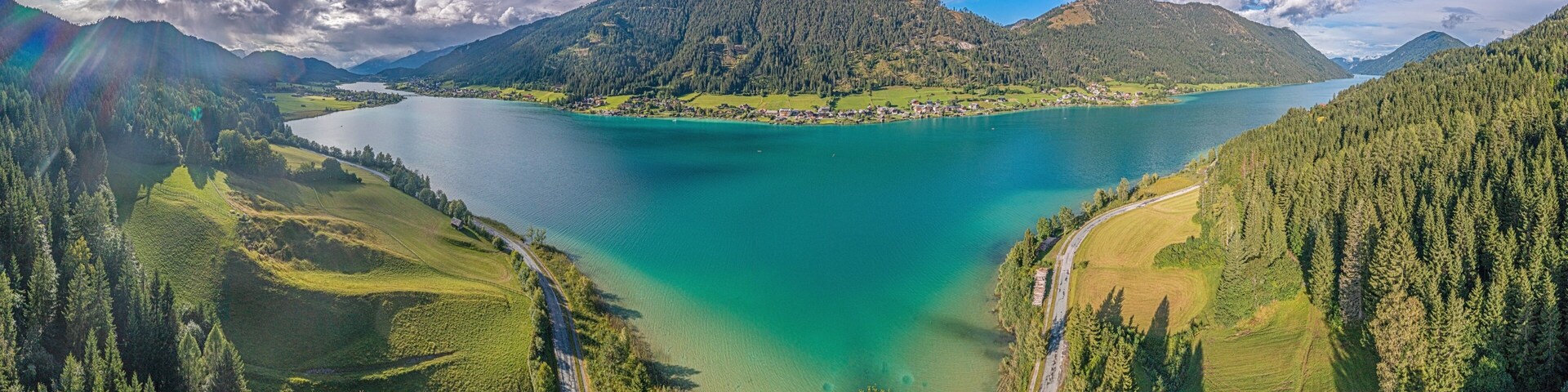 A lake surrounded by forested hills and a winding road.